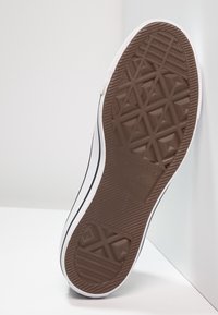 Semelle de chaussure en caoutchouc marron avec un motif de bande de roulement géométrique, des flancs blancs et des lignes d'accent noires. Présente une marque "Converse All Star".