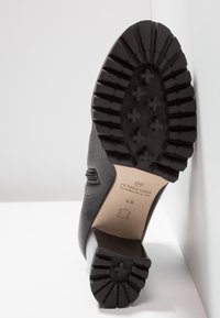 Chaussure noire en cuir avec une tige texturée, un bout lisse et une semelle en caoutchouc à rainures. La semelle intérieure comporte une étiquette de marque et des informations sur la taille.