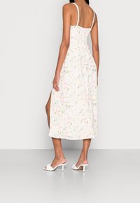 Vestido maxi floral en rosa claro con patrón de flores en tonos pastel, tirantes finos, espalda fruncida, abertura lateral, combinado con mules blancos de tacón.