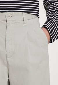 Pantalons en tissu gris clair avec une coupe décontractée, dotés de poches avant, d'une fermeture à bouton, et d'une texture diagonale subtile.