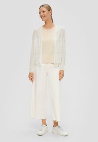 Leichter, transparenter weißer Cardigan über einem beigen Top, kombiniert mit weiten weißen Hose und weißen Sneakers, neutrale Farbpalette, glatte Textur.