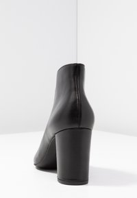 Bottine en cuir noir à texture lisse, bout arrondi et talon haut épais. Présente des coutures minimales le long des bords.