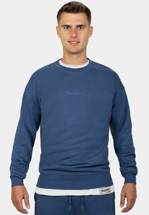 Blue sweatshirt in a soft fabric, featuring ribbed cuffs and hem, embroidered logo on the chest, and layered design with a white shirt underneath.