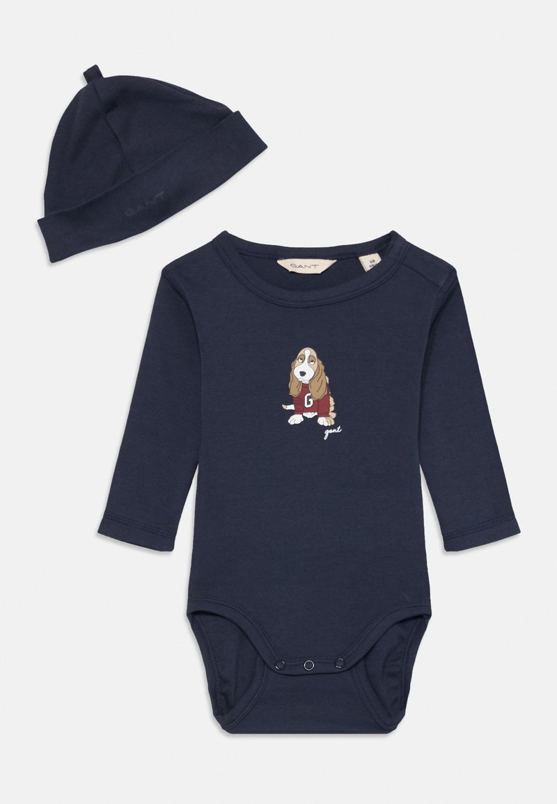 Tamsiai mėlynas medvilninis kūdikio bodis su ilgomis rankovėmis ir spaudėmis, su basset hound iliustracija ir žodžiu "gand." Pridedama atitinkama skrybėlė.