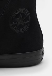 Must musta kõrge värvitud king, millel on ümmargune, reljeefne "Converse All Star" logo välisküljel ja tekstureeritud must kummi talla.