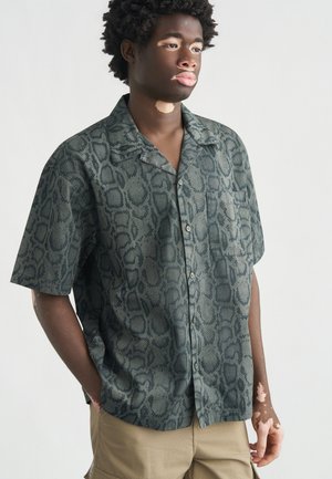 Camicia a maniche corte con bottoni in verde con motivo a stampa di serpente strutturata. Presenta una tasca sul petto e una vestibilità rilassata.
