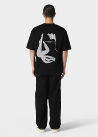 Sort T-shirt med et hvidt grafisk motiv af hænder og striber på ryggen. T-shirten har en afslappet pasform og er kombineret med løse sorte bukser.