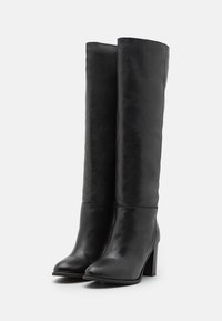 Bottes en cuir noir jusqu'au genou avec bouts carrés et talons épais, présentant une texture lisse et un design minimaliste, sans aucune pièce métallique visible.