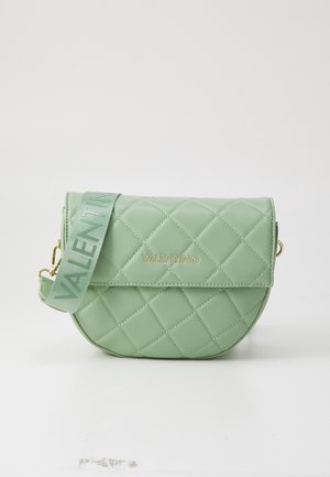 Kvadrātveida zaļa sintētiska rokassoma ar apaļu formu, zelta logo un regulējamu siksnu ar zīmola nosaukumu saskaņotā krāsā.