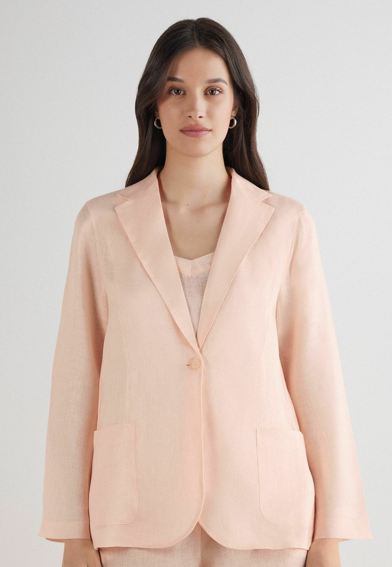 Světle růžový lněný blazer s klopovými límci, zapínáním na jeden knoflík a dvěma předními kapsami. Hladká textura a volný střih.