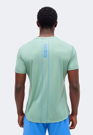 Férfi mentazöld rövid ujjú ingben, melyen függőleges kék „BORG” felirat van a háton, világoskék rövidnadrággal párosítva.