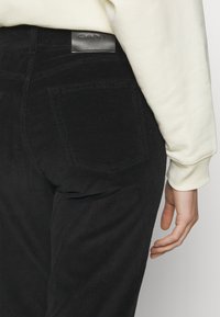 Μαύρο παντελόνι κοτλέ με κατακόρυφες ραβδώσεις, με ένα δερμάτινο ταμπελάκι που αναγράφει "GANT" στη μέση στο πίσω μέρος και δύο πίσω τσέπες ορατές.