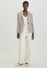 Vaaleanharmaa pellavapuku, jossa on yksi nappi, valkoisen V-pääntien paidan päällä, yhdistettynä leveälahkeisiin kermaanvärisiin housuihin ja vaaleisiin liukuvasti pysyviin kenkiin.