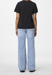 Svart kortärmad t-shirt i kombination med ljusblå vida jeans, med en klassisk denimtextur och detaljer med sömmar på bakfickorna.