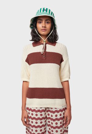  Gebreide polo trui met bruin en crème strepen, voorzien van een kraag en knoopsluiting. Gecombineerd met gestreepte broeken in rood en crème.