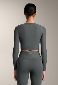 Szürke bordázott hosszú ujjú crop top, kerek nyakkivágással, amelyet magas derékú leggingsszel párosítottak. Az anyag simának tűnik, enyhe fénylő hatással.