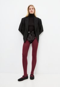 Blazer negro sobre un cuello de tortuga negro, combinado con pantalones cortos de lentejuelas, medias burdeos y zapatos negros con correa.