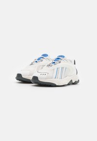 White athletic shoes feature a mesh and synthetic upper with blue accents, a chunky sole, and three vertical stripes on the side.