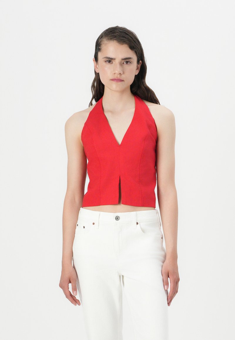 Haut court rouge à dos nu avec un décolleté en V profond, ajustement cintré et fente à l'avant, associé à un jean blanc taille haute. Tissu lisse, lignes épurées.