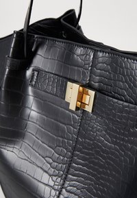 Borsa in finta pelle di coccodrillo nera con chiusura in metallo dorato, forma strutturata e texture liscia con un leggero effetto lucido.
