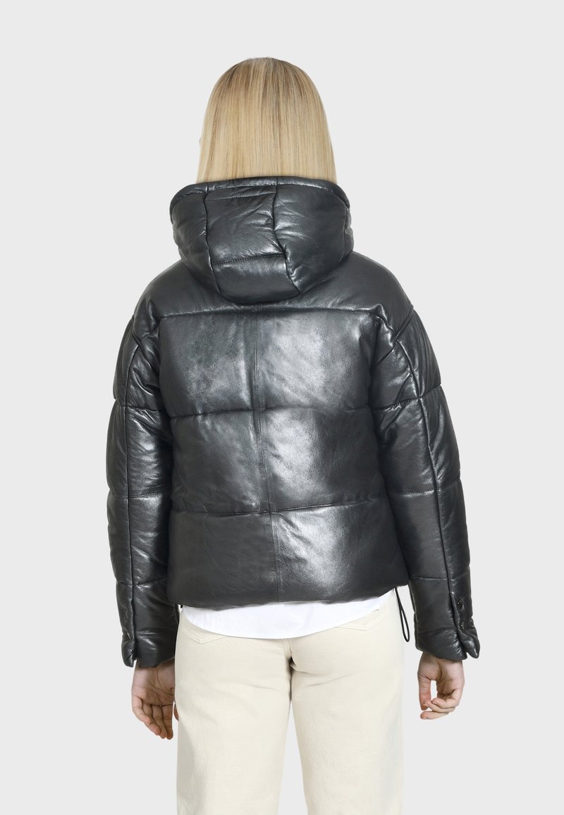 Schwarze Pufferjacke aus glänzendem Leder mit Kapuze, im boxy Design, gestepptem Look und elastischen Bündchen, getragen über einem leichten Shirt.