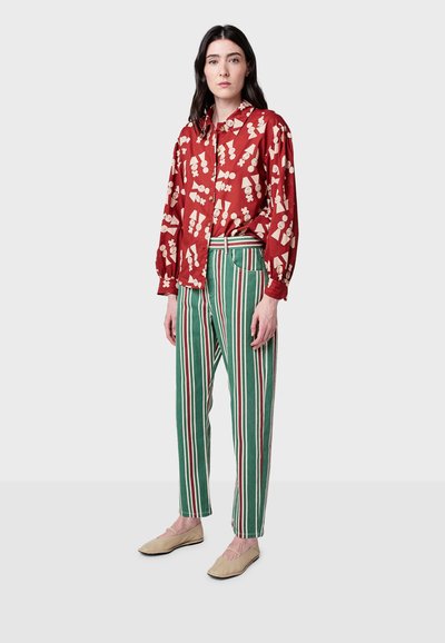 Červená blúzka s krémovými vzormi, balónové rukávy a zelené pruhované nohavice. Oblečenie dopĺňajú ploché béžové topánky. Obe kúsky sú vo voľnom strihu.