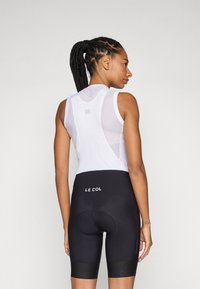 White sleeveless cycling jersey with mesh panels and black cycling shorts featuring "LE COL" branding on the waistband and thighs.