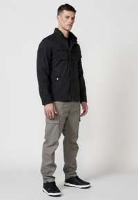 Jachetă neagră cu guler în picioare, două buzunare pe piept și închidere cu fermoar. Asortată cu pantaloni cargo gri deschis și adidași negri.