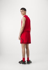 Raudona be rankovių sportinė palaidinė su atitinkamomis krepšinio šortais, turinčiais juodus akcentus ir išskirtinį raštą; dėvima su juodais ir raudonais sportbačiais.