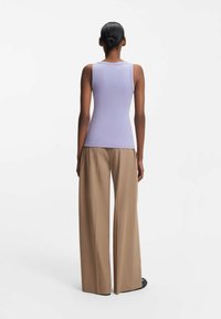 Lilat hihattomat toppi, jossa on istuva malli, yhdistettynä väljään beigen väriseen housuihin. Sileä pinta, vähäiset ompelusaumat ja litteät saumat.