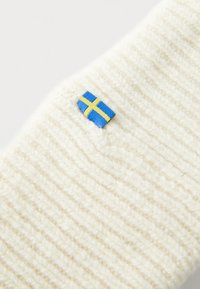 Witte ribgebreide stof van dichtbij met een klein genaaid Zweeds vlaggetje in een blauw en geel kruispatroon.
