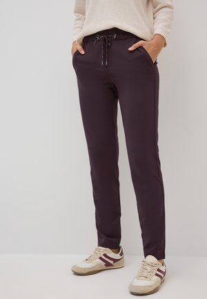 Pantalons de jogging violets foncés avec une taille élastique et un cordon de serrage, dotés de poches latérales et d'une coupe slim. Associés à des baskets beiges.
