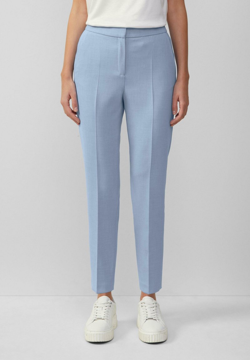 Pantalon bleu clair sur mesure avec une texture lisse, doté d'un devant plat et d'une coupe slim, associé à des baskets blanches.