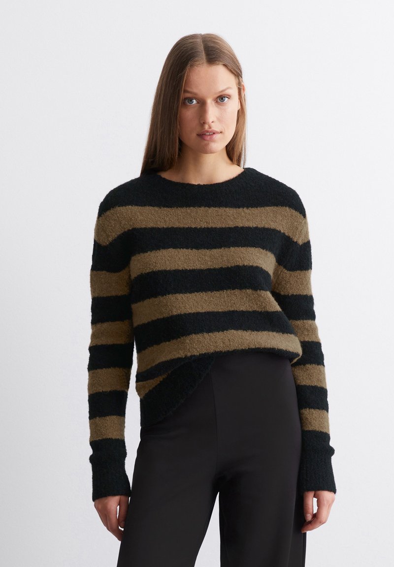 Pull rayé en noir et vert olive, texture pelucheuse, col rond et coutures d'épaule tombantes. À associer avec un pantalon noir ajusté.