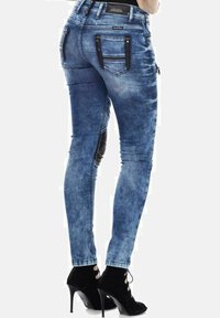 Skinny jeans in vervaagd blauw denim, met ritsvakjes en decoratieve stiksels. Zachte textuur met een slanke pasvorm, gecombineerd met zwarte hakken.
