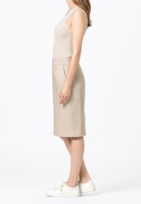 Gonna beige al ginocchio con davanti piatto, tasche laterali, realizzata in tessuto liscio. Abbinata a una canotta a coste chiara e sneakers bianche.