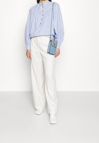 Blusa a strisce azzurre con chiusura a bottoni, maniche a palloncino; abbinata a pantaloni bianchi a gamba larga e una piccola borsa blu. Scarpe con tacco a blocco bianche.