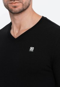 T-shirt nera con scollo a V realizzata in tessuto morbido, con un piccolo logo bianco sul lato sinistro, dal design aderente e collo pulito.