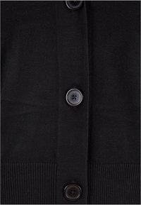 Cardigan noir avec une texture tricotée lisse, un ourlet côtelé et quatre boutons ronds. Les boutons sont sombres avec une finition mate.