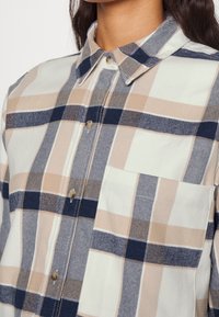 Overhemd met knopen en een geruit patroon in beige, marineblauw en crème kleuren. Gemaakt van zacht materiaal, het heeft een borstzak en een kraag.