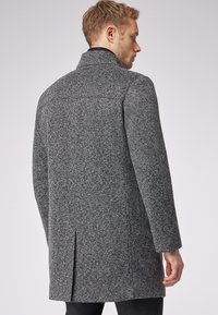 Grau Hahnentritt-Mantel mit Stehkragen, taillierter Passform und Rückenschlitz für Bewegungsfreiheit. Hergestellt aus strukturiertem Wollmischgewebe.