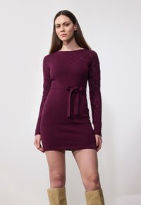 Sügavburgundi tooni kootud kleit pikkade teemantmustritega varrukatega, kitsas bodice ja sobiv vöö talje ümber. Sile tekstuur, põlve kõrgune pikkus.
