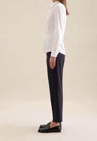 Witte langebloezende shirt met een knoopsluiting, gecombineerd met donkere marineblauwe slim-fit broek en zwarte leren loafers.