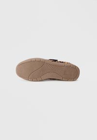 Sneaker med leopardmønster og en fleksibel svart stoffoverdel, med en teksturert beige gummisåle som har grep-mønstre og dempingselementer.