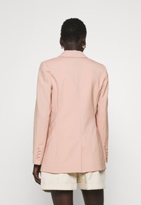 Blazer rosa con un diseño ajustado, solapas muesca y puños abotonados, combinado con pantalones cortos crema, que exhiben líneas minimalistas y una estructura a medida.