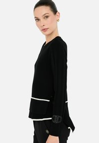 Maglione nero a coste con dettagli bianchi all'orlo e alle maniche. Presenta un collo a V, spacchetti laterali e un dettaglio del logo ricamato sulla manica.