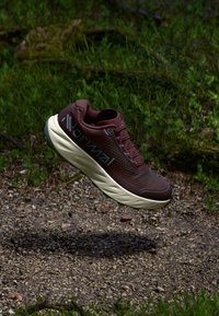Running shoe in maroon mesh upper with beige sole, featuring lightweight design, textured fabric, and prominent branding on the side.