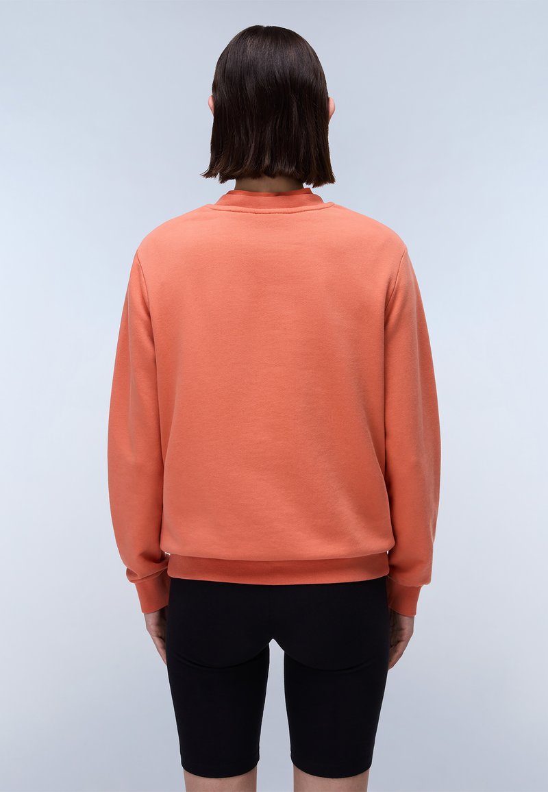 Felpa arancione con scollatura rotonda, maniche lunghe e polsini a costine. Abbinata a pantaloni shorts neri aderenti. Tessuto liscio, design casual.