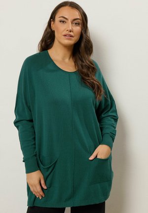 Skovgrøn oversized sweater med rund halsudskæring, ribkantede manchetter og to frontlommer. Blød tekstur og afslappet pasform.