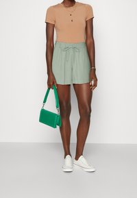 Light brown fitted t-shirt, loose light green shorts with elastic waistband and tie, white sneakers, green handbag with a structured design.